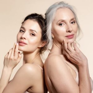 Elderly and young women with smooth skin and natural makeup standing back-to-back